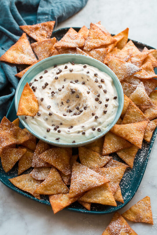 _*Cannoli Dip*_ /Cannoli Dip – A party-friendly spin on a widely popular Italian dessert that’s turned into a perfectly dip-able treat. It’s made with rich ricotta, fluffy whipped cream, sweetened with fine powdered sugar and dotted with tiny dark chocolate chips. A fun and easy way to make cannoli!/ #CannoiliDipRicottaDip #Desserts #TartsAndPastries #TreatsAndSnacks #ChocolateChips #Cream #Mascarpone #PowderedSugar #Ricotta Prep: 10 minutes. Ready in: 10 minutes. INGREDIENTS: 1: 15 oz whole milk ricotta cheese, strained*. 2: 3/4 cup (80g) powdered sugar, plus more for dusting if desired. 3: 1 tsp fresh lemon juice. 4: 1/2 tsp vanilla extract. 5: 1/4 tsp cinnamon, plus more for dusting. 6: 1/2 cup heavy cream. 7: 1/2 cup mini semi-sweet chocolate chips, plus 1 Tbsp for garnish. 8: 1/3 cup chopped unsalted pistachios, plus 1 Tbsp for garnish (optional). INSTRUCTIONS: 1: In a mixing bowl using an electric hand mixer whip heavy cream until very stiff peaks form. 2: In a separate mixing bowl using a spatula, stir together ricotta, powdered sugar, lemon juice, vanilla extract, and cinnamon. 3: Fold whipped cream into ricotta mixture then fold in chocolate chips and pistachios of using. 4: Serve topped with remaining chocolate chips and optional pistachios , dusted lightly with powdered sugar if desired. 5: Serve with homemade cannoli chips**, crackers such as graham crackers, waffle crisps or Anna's orange crackers, or fried flour tortilla chips or wonton chips. Notes: *To strain I simply lay the ricotta over several layers of paper towels, then wrap and squeeze to remove excess moisture. You want to remove enough moisture that the Ricotta should hold it's shape pretty well so you may want to do this step twice. Pistachios and cannoli chips not included in nutrition estimate as these are optional. Homemade Cannoli Chips To make cannoli cheese make one batch of dough from this recipe (you don't need the egg white, just the whole egg). Divide rested dough into 2 equal portions. Roll each portion into a very thin rectangle on a floured surface, about 14 by 12-inches. Cut into 2-inch thick strips then cut each strip into 2-inch rectangles. Deep fry in preheated 350 degree oil in batches about 12 at a time until golden brown on each side, turning halfway through (about 15 seconds on each side). Use a spider strainer to remove then transfer to paper towel lined plate to drain. Repeat with all of the dough.