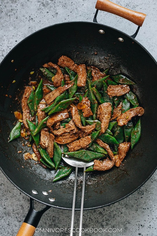 _*Beef and Flat Bean Stir Fry*_

/Beef and flat bean stir fry is a quick main dish featuring juicy tender beef and thick romano beans brought together with a fragrant brown sauce./

[To make this dish gluten-free, use tamari to replace soy sauce, and use dry sherry instead of Shaoxing wine.]

Prep Time: 15 minutes
Cook Time: 10 minutes
Total Time: 25 minutes
Servings: 2 to 3 servings

_Ingredients_ 
Meat and Marinade: 
300 g (10 oz) boneless flank steak , skirt steak, or other cut (*see footnote 1)
1 teaspoon soy sauce
1/4 teaspoon salt
1 teaspoon peanut oil (or vegetable oil)
1 teaspoon cornstarch

Sauce:
2 tablespoons chicken broth (or beef broth)
1 tablespoon Shaoxing wine (or dry sherry)
1 tablespoon soy sauce
1/2 teaspoon dark soy sauce (*footnote 2)
1/4 teaspoon sugar
1 teaspoon cornstarch

Stir-fry:
300 g (10 oz) flat beans , cut to 1” (1.5 cm) pieces
1 tablespoon peanut oil (or vegetable oil)
1 clove garlic , sliced
1/2 thumb ginger , sliced

Instructions:
1: Slice the beef against the grain into 0.5 cm (1/4 inch) thick slices or 1-cm (1/2 inch) sticks. Transfer to a small bowl. Add soy sauce and salt (*Footnote 1). Gently mix well by hand until all the slices are coated. Add the peanut oil and cornstarch. Mix again to combine evenly. Marinate for 15 minutes while preparing the other ingredients.

2: Combine all the ingredients for the sauce in a medium-sized bowl. Mix well.

3: Bring a medium pot of water to a boil. Add the flat beans and boil for 5 minutes, or until the beans turn tender. Drain and run the beans with tap water for a few seconds, to stop cooking. Then drain again thoroughly and set aside.

4: Heat oil a large skillet or a wok until hot. Swirl to coat the bottom. Spread the steak in a single layer. Allow to cook without touching for 30 seconds, or until the bottom side is browned. Flip to cook the other side for a few seconds. Stir and cook until the surface is lightly charred and the inside is still a bit pink. Transfer to a plate.

5: The pan should still have some oil left. If not, add 2 teaspoons of oil. Add the garlic and ginger. Stir a few times to release the flavor and fragrance.

6: Add the flat beans to the pan. Stir and cook for 1 minute. Add the beef back to the pan.

7: Stir the sauce again to dissolve the cornstarch completely and pour it into the skillet. Cook and stir until the sauce thickens. Transfer everything to a plate immediately. Serve hot as a main dish.

Notes:
1: If you need to use a cheaper or tougher cut of beef, for example, chuck, brisket, or round roast, add 1/4 teaspoon of baking soda to the marinade and marinate the beef for 30 minutes before cooking. This method tenderizes the beef and will create a very juicy result.

2: Dark soy sauce will add an appetizing dark color to the sauce with a hint of caramel taste, but you can skip it if you don't have it. If you skip the dark soy sauce, you can add 1/2 teaspoon molasses to enhance the flavor.
