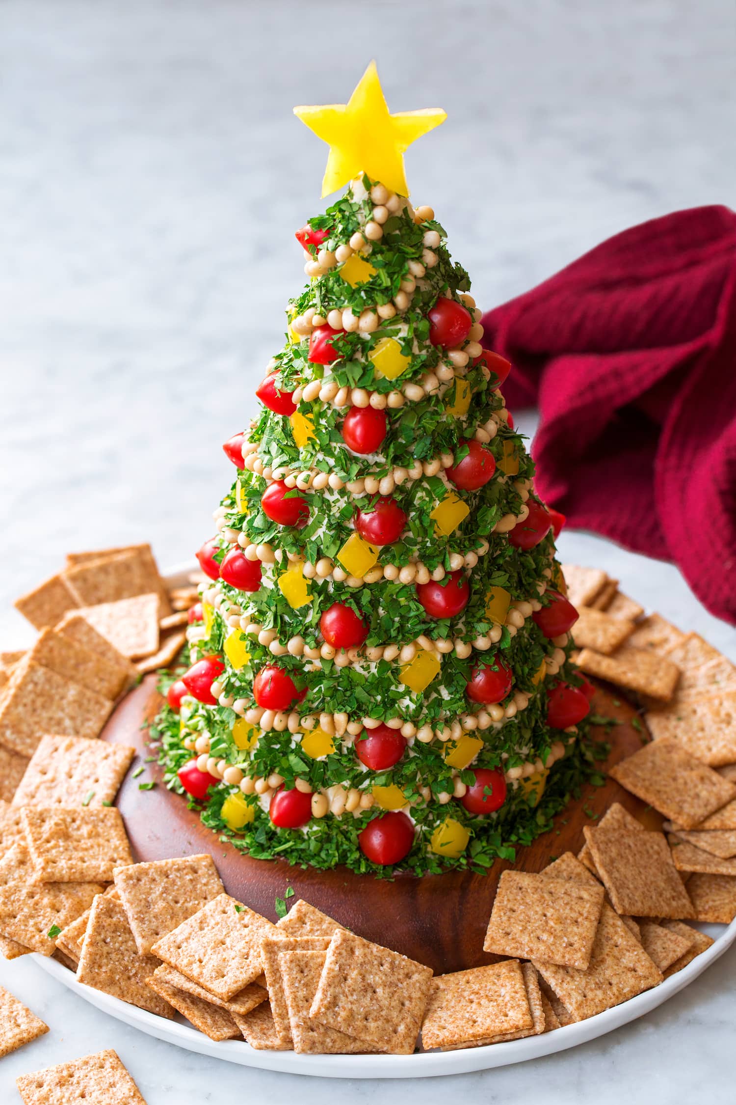 _*Christmas Tree Cheese Ball*_ /A festive and delicious Christmas Tree Cheese Ball! A Christmas appetizer made with rich cream cheese, sharp white cheddar, flavorful herbs and fresh vegetables. It’s a holiday party favorite and a tasty twist on the classic cheese ball./ #BellPeppers #CheddarCheese #CreamCheese #Dill #GarlicPowder #GreenOnions #Parsley #PineNuts #Tomatoes Servings: 16 Ready in: 45 minutes Prep: 45 minutes Ingredients: 3 (8 oz each) pkgs. cream cheese, softened to room temp 16 oz. sharp white cheddar cheese*, shredded (4 cups) 3/4 cup sliced green onions (green tops only) 2 tsp dried dill or 1 Tbsp chopped fresh dill 3/4 tsp garlic powder Salt and black pepper, to taste 1 pretzel rod (optional for added stability) 3/4 cup finely chopped fresh parsley 1 cup mini grape tomatoes or chopped red bell pepper 1 yellow bell pepper, 1 star cut, 1/2 cup chopped 1/2 cup pine nuts Savory crackers, for serving Instructions: *1.* In the bowl of an electric stand mixer using a paddle attachment cream together blocks of cream cheese until smooth. Scrape down bowl. *2.* Add in white cheddar cheese and green onions, then sprinkle over dill, garlic powder and season with salt and pepper to taste (I use about 1/2 tsp each but this is personal preference, saltiness of cheese may vary and you may not want as much). *3.* Remove paddle then smooth mixture out into bowl in an even layer spreading mixture up the sides of the bowl as well (this is for faster more even chilling). Cover and chill 1 hour. *4.* Remove mixture from fridge then cover hands with food grade gloves or wash well. Shape mixture into a tall cone shape like a "Christmas tree" if using a pretzel rod shape the mixture around the pretzel using it as the center for added stability (it should not show through anywhere). Tree should be about 10 inches tall. Place cheese "cone" on a serving plate and press down so it sticks, reshaping as needed. *5.* Next add mini grape tomatoes (can cut in half if they are too large to press in) pressing them randomly over "tree" then add bell pepper pieces randomly around. Add a "ribbon" of pine nuts wrapped around the tree starting at the top, press them in so they stick well. *6.* Then take a handful of parsley, tilt tree and press parsley into "tree" coating entire cheese ball. Last insert a toothpick into the bell pepper star and insert at the top of the tree. *7.* Serve shortly after preparing or keep chilled in the fridge in an airtight container. Notes: *8 oz. sharp white cheddar with 8 oz. Havarti would also be a delicious option. If you want a softer cheese ball let it rest at room temperature for 30 minutes before serving, though don't keep at room temp longer than 2 hours. Another option is to warm individual leftover servings on a microwave safe dish for 10 seconds at 50 percent power to soften slightly. Crackers not included in nutrition estimate.
